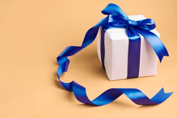 White gift with blue ribbon on a biege background — Stock Photo, Image