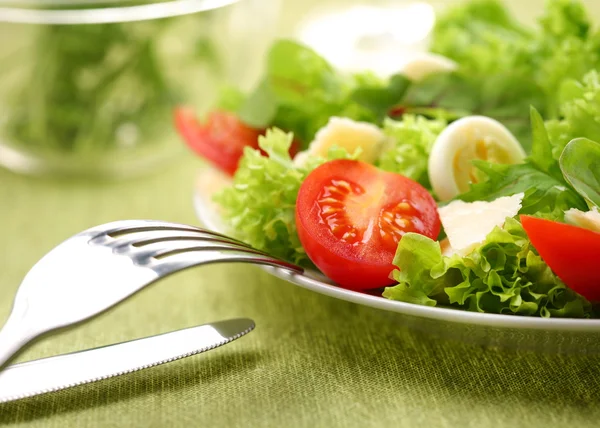 Ensalada fresca con tomate y huevos de codorniz en un tazón blanco sobre una mesa verde —  Fotos de Stock