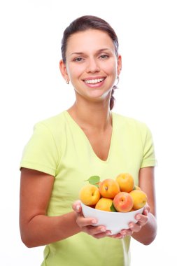 Smiling young woman keeping full bowl with apricots in her hands. Isolated clipart