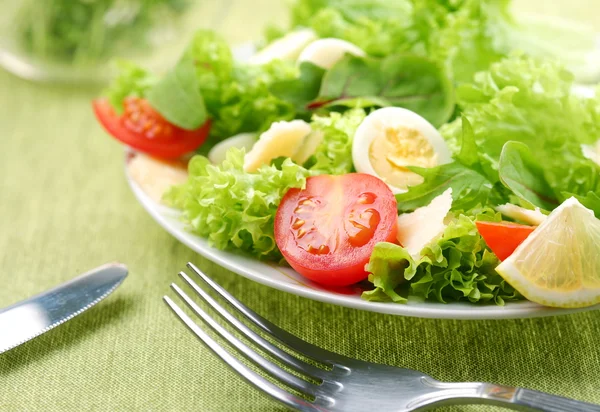 Salade fraîche avec tomates et oeufs de caille dans un bol blanc sur une nappe verte — Photo