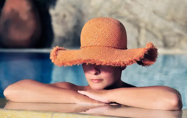 Attractive young woman in hat resting by the side of a pool — Stock Photo, Image