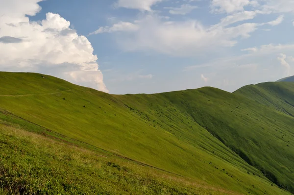 Hegyi ridge lejtők borított zöld fű és a felhős kék ég — Stock Fotó
