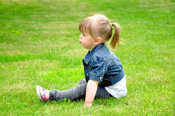 Little girl sits on the grass — Stok fotoğraf
