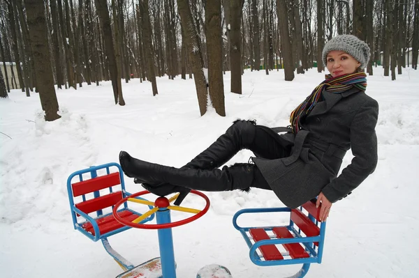 La niña se sienta en una rotonda infantil en el parque en el invierno — Foto de Stock
