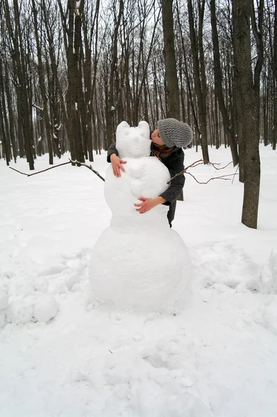 La muchacha abraza y besa al monigote de nieve grande en el parque en invierno —  Fotos de Stock