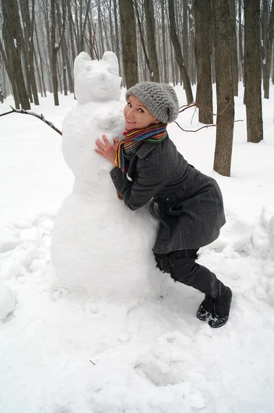 A menina abraça o grande boneco de neve no parque no inverno — Fotografia de Stock