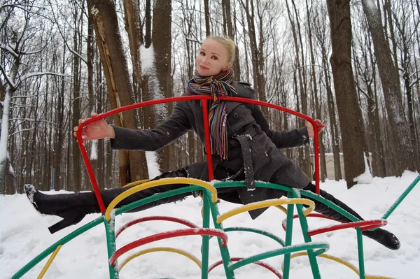 La muchacha se sienta sobre el cordel al diseño infantil en el parque en invierno —  Fotos de Stock