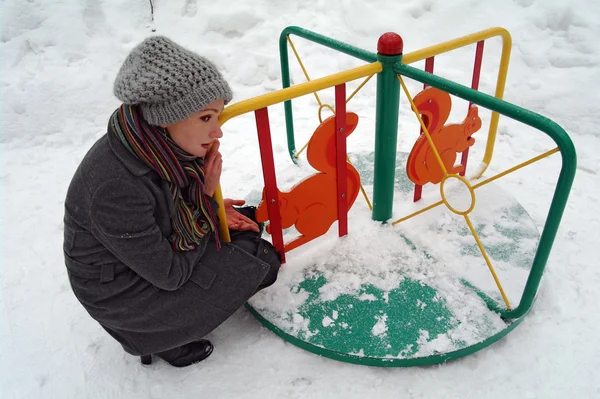 La fille s'assoit autour d'un rond-point pour enfants dans le parc en hiver — Photo