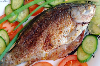 Fried fish the Crucian on a plate, with tomatoes, cucumbers, onions and lime clipart