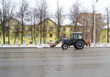 The snow-removing tractor goes on the way to a background of the yellow hou clipart