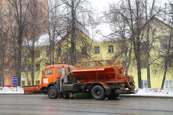 Der LKW reinigt die Straße von Schmutz und Schnee gegen das gelbe Haus Stockbild