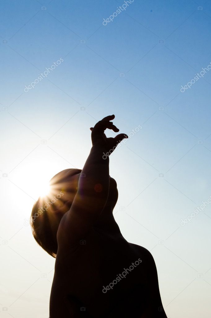 Adorable child silhouette over sunshine pointing up