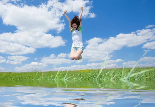 Jumping happy women on field with reflection in the water — Stock Photo, Image
