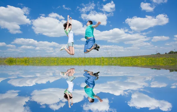 Saltando feliz pareja en el campo con la reflexión en el agua — Foto de Stock