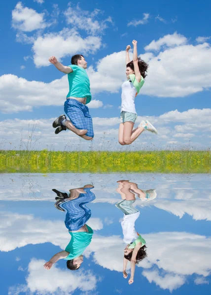 Jumping happy couple on summer field with reflection in the wat — Stock Photo, Image