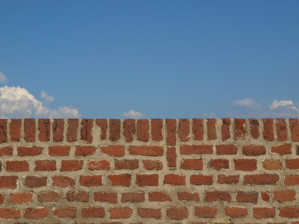 A wall with blue sky with clouds behind