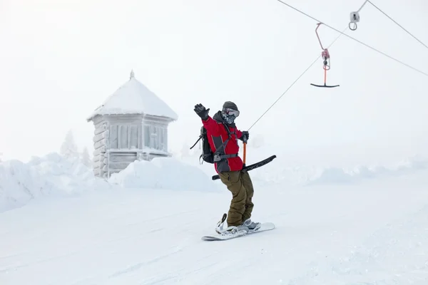 Snowboarder rises up the mountain on sky-lift — Stock Photo, Image