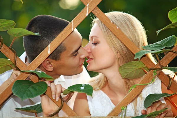 Young happy couple kissing at wooden lattice — Stock Photo, Image
