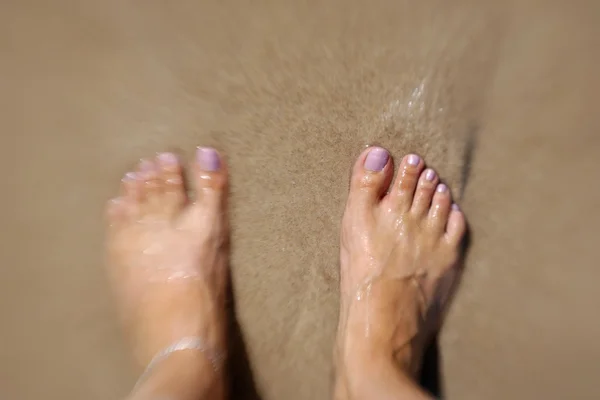 Pés femininos na água e na areia — Fotografia de Stock