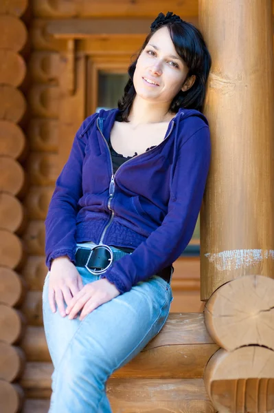 Νεαρή γυναίκα ευτυχισμένη που αναπαύεται μπροστά από ένα ξύλινο εξοχικό σπίτι — Φωτογραφία Αρχείου