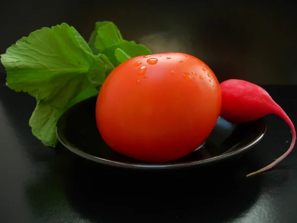 The red tomato with radish on a black plate — Stock Photo, Image
