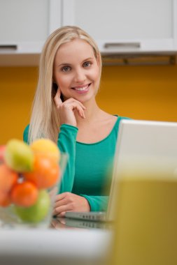 Beautiful young woman wotking on laptop in her kitchen clipart