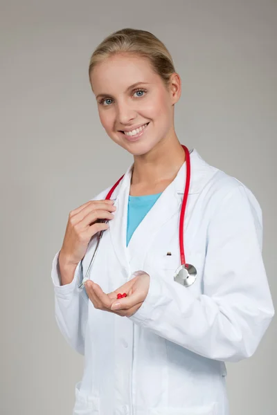 Médico sosteniendo una pequeña píldora roja en sus dedos — Foto de Stock