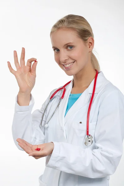 Médico segurando uma pequena pílula vermelha em seus dedos — Fotografia de Stock