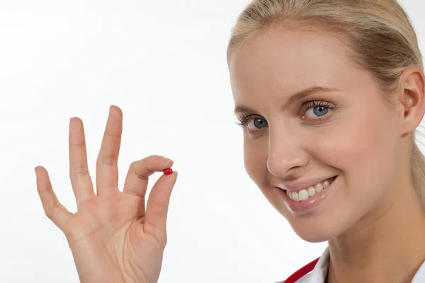 医者は彼女の指で小さな赤い錠剤を保持 — ストック写真