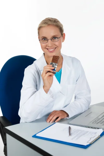Mooie vrouwelijke arts chocolade eten terwijl u werkt in haar — Stockfoto
