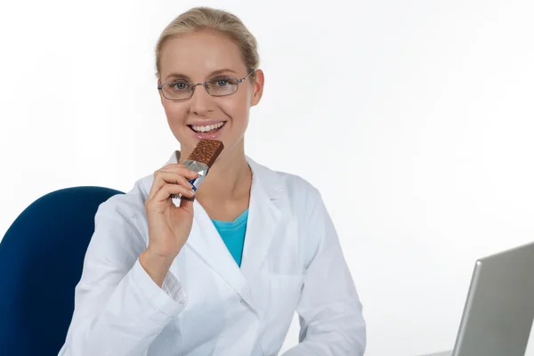 Όμορφη γυναίκα γιατρό που τρώει σοκολάτα, ενώ εργάζονται σε αυτήν της — Φωτογραφία Αρχείου