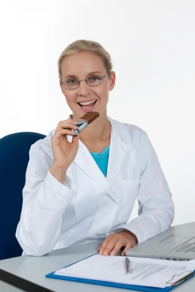 Schöne Ärztin, die Schokolade isst, während sie in ihrem — Stockfoto