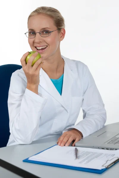 Médica bonita comendo uma maçã enquanto trabalhava nela fora — Fotografia de Stock