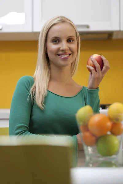 美丽的年轻女子，在她的厨房拿一个苹果 — 图库照片