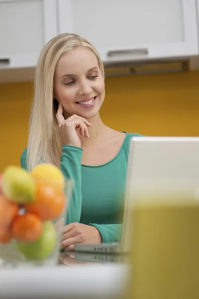 Hermosa mujer joven wotking en el ordenador portátil en su cocina —  Fotos de Stock