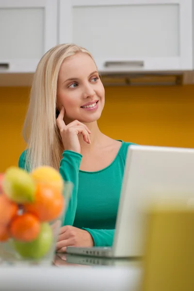Beautiful young woman wotking on laptop in her kitchen — Stock Photo, Image