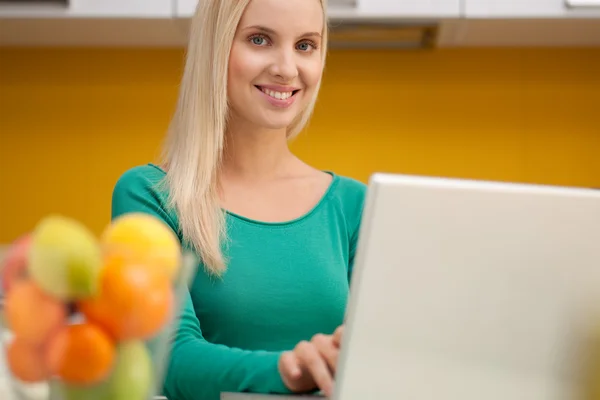 Hermosa mujer joven wotking en el ordenador portátil en su cocina — Foto de Stock