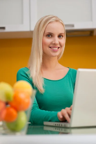 Mooie jonge vrouw wotking op laptop in haar keuken — Stockfoto