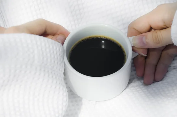 Vista de cerca de las manos sosteniendo una taza de café negro en el fondo de la túnica blanca — Foto de Stock