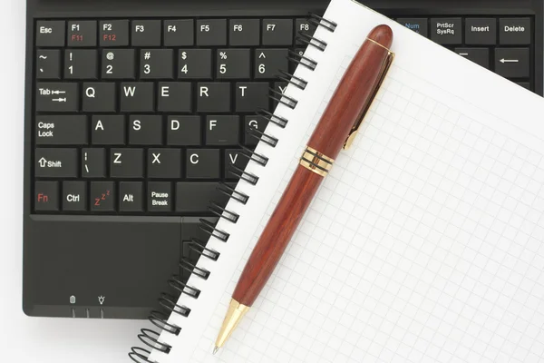 Ручка и спиральный блокнот на черной клавиатуре ноутбука — стоковое фото
