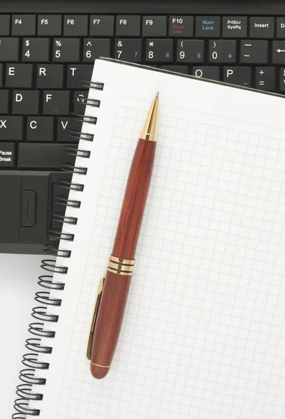 Ручка и спиральный блокнот на черной клавиатуре ноутбука — стоковое фото