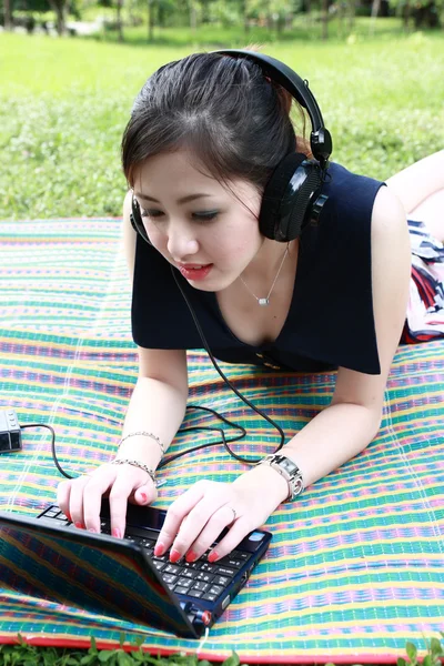 Chica con un ordenador portátil y auriculares en el parque — Foto de Stock