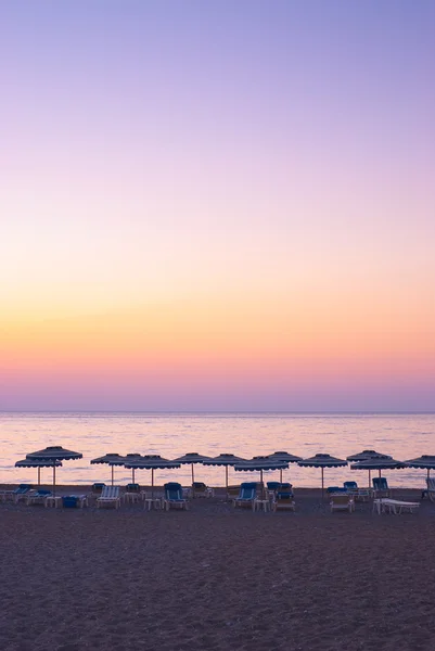 stock image Beautiful sunset at the sea and sunshades on the beach