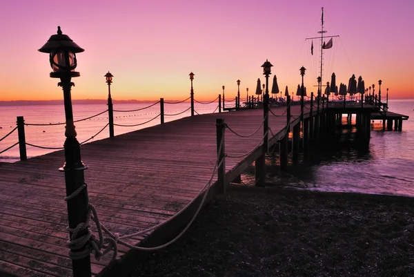 Wooden pier lighted by pink sunrise glow — Stock Photo, Image
