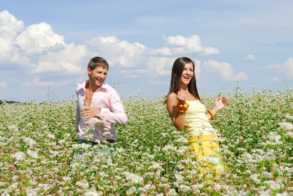 Ungt par spelar på fält av blommor i solig dag — Stockfoto