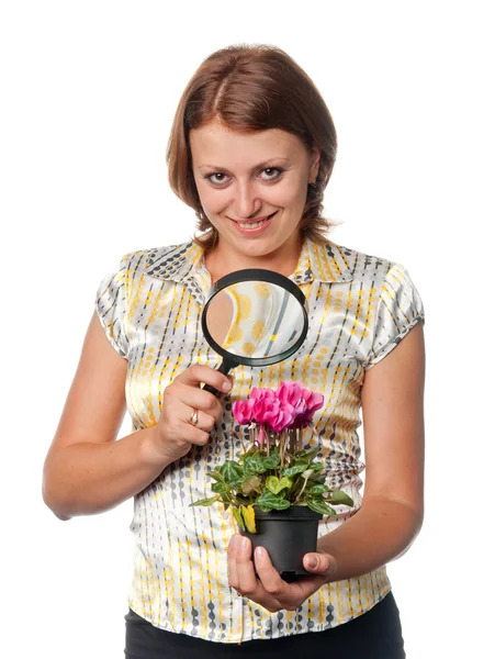 Smiling girl considers cyclamens through a magnifier — Stock Photo, Image