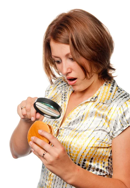 Surprised girl considers a hamburger through a magnifier — Stock Photo, Image