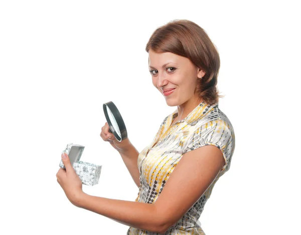 Smiling girl looks at a gift through a magnifier — Stock Photo, Image