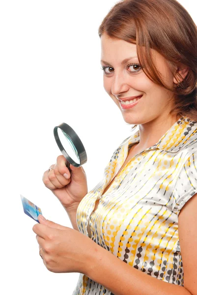 Chica sonriente considera una tarjeta de crédito a través de una lupa — Foto de Stock