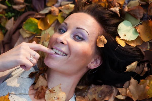 Chica sonriente acostada en hojas Imagen de archivo